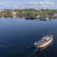 Väyläalus S/s Saimaa lipuu Olavinlinnan edustalla. Vesi on tyyni ja aurinko paistaa puolipilvisellä taivaalla.