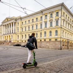 Valtioneuvoston linna. Etualalla mies ajamassa sähköpotkulaudalla.