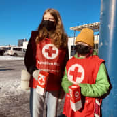 Kaksi lasta pitelee Punaisen Ristin keräyslippaita käsissään.