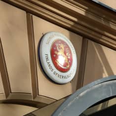A plaque with a red lion on a door saying "Finnish consulate" in Finnish and Swedish.
