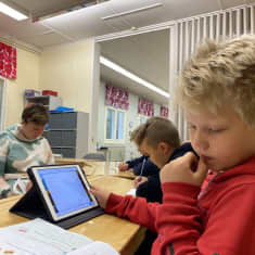 Kolmasluokkalaisia poikia oppitunnilla, etummaisella on tabletti ja oppikirja.