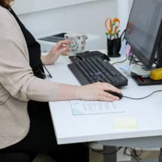 hoitaja istuu tietokoneen ääressä käsi tietokoneen hiirellä.