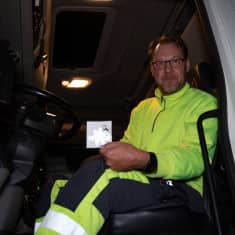 Mika Vaittinen istuu rekan nupissa ja pitää kädessään heijastinta.