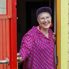 Annu Sankilampi seisoo hymyillen taidekeskus Haihatuksen punaiseksi maalatun oven suussa.