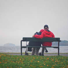 Iäkäs pariskunta selin kuvaan istumassa puiston penkillä järven rannassa