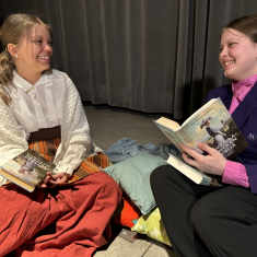 Abiturientit Eveliina Isotalo ja Emmi Martin istuvat lattialla näytelmän lavasteissa ja katsovat toisiaan.