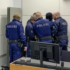 Vantaan vankilan sellisurman oikeudenkäynnissä toinen syytetty nousi ylös oikeudenkäynnin alussa ja poliisit rauhoittivat häntä.