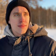 Pakkaskeliin pukeutunut Johannes Takamäki katsoo vähän ohi kamerasta. Taustalla luminen järvenranta. Aurinko valaisee puolet kasvoista.