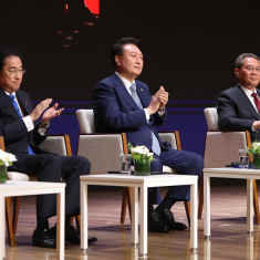 Tre asiatiska herremän i kostym sitter i stolar på en rad och applåderar. Det är Japans, Kinas och Sydkoreas representation.