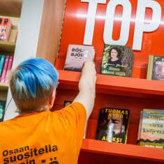 Myyjä laittaa kirjoja kirjakaupan top 10 -hyllyyn.