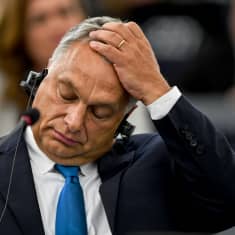 Ungerns premiärminister Viktor Orban reagerar.  Han har fört sin vänsterhand till pannan och blundar. 