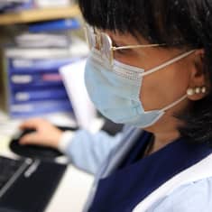 Sairaanhoitaja työskentelee tietokoneella kasvomaski kasvoillaan.