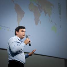 Thomas Piketty puhuu mikrofoniin. Taustalla esitys, jossa näkyy maailman kartta.