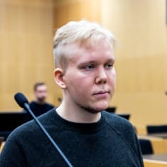 Aleksanteri Kivimäki at Western Uusimaa District Court. Young man with blond hair, chubby cheeks, beard under his chin wearing a dark sweatshirt.