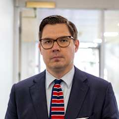 Silmälasipäinen mies seisoo valoisassa aulassa.