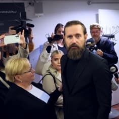 Mustiin pukeutunut laulaja Lauri Tähkä asianajajansa ja median ympäröimänä oikeustalon aulassa.