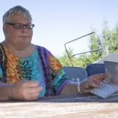 Rääkkyläläinen Sirpa Laurimo istuu terassipöydän ääressä ja katsoo Veäjän viisumia.