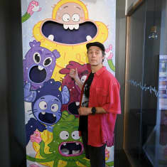 Punapaitainen mies näyttää peukalollaan takanaan olevaa julistetta, jossa on lasten animaatiosarjan hahmoja.