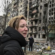 Nainen suree tuhoutuneen kerrostalon edessä Kiovassa.