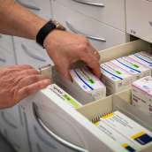 Reseptilääkkeitä lääkelaatikostossa apteekissa. Käsi tarttumassa yhteen lääkerasiaan.