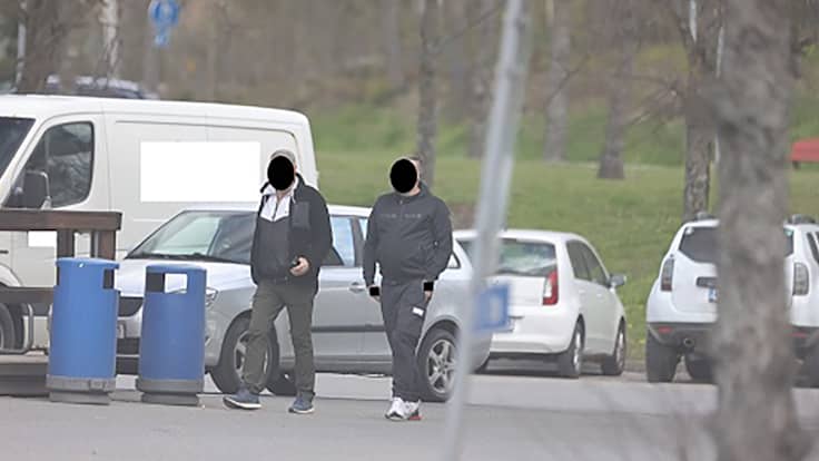 Två personer ses gå längs en väg vid sidan av parkerade bilar. Deras ansikten är digitalt maskerade för att skydda identiteterna.