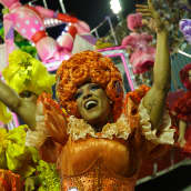 Rion karnevaalien esiintyjiä punaisessa, oransseissa ja keltaisissa röyhelöasuissa tanssivat.