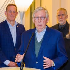Mitch McConnell Mäntyniemessä, seisoo ja katsoo kameraan, taustalla senaattoreja.