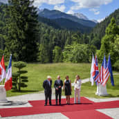 Valtion johtajia kumppaneineen seisoo punaisella matolla vuoristoisessa maisemassa.