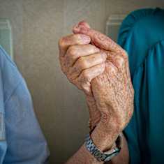 Photo shows two old people holding hands.