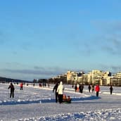 Ihmisiä kävelyllä aurinkoisena pakkaspäivänä Lahden Vesijärven jäällä. Lapsia vedetään pulkassa, hiihtäjiä jäätien vieressä