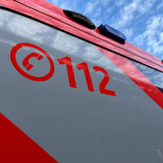 Osa auton kyljestä, jossa on punaiset ja harmaat teippaukset. Keskellä on punainen puhelinluurin kuva ja numero 112.