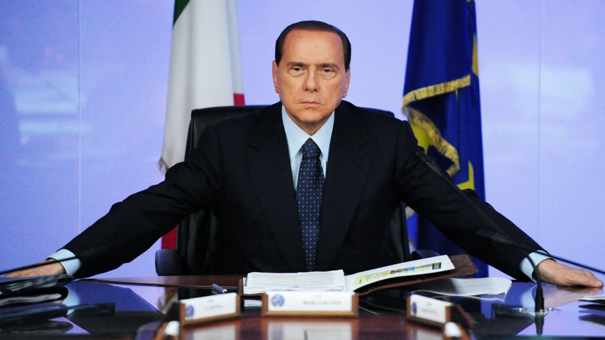 Silvio Berlusconi istuu pöydän ääressä.