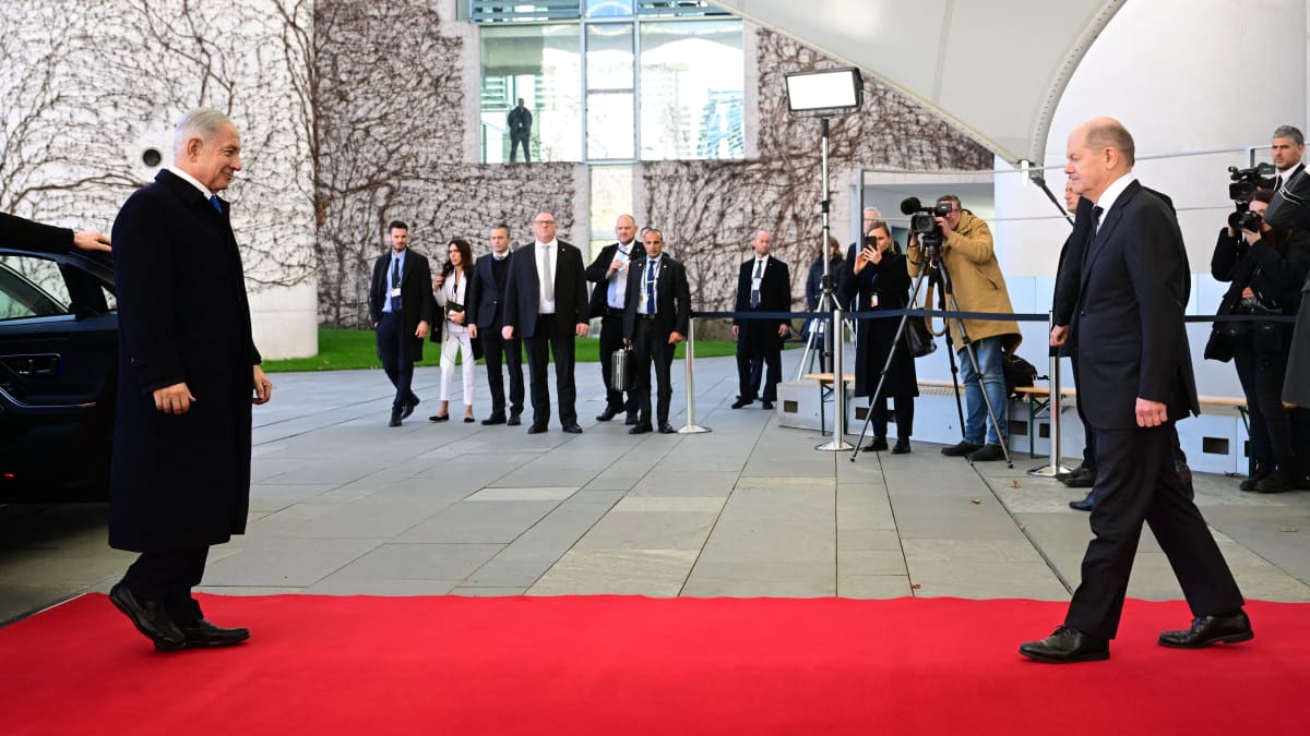 Kaksi poliitikkoa kävelee toisiaan kohti punaisella matolla. Taustalla median edustajia.