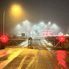 A closed crossing at the eastern border at night in the fog, with bright lights and a closed gate.