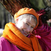 Oranssiin ja pinkkiin pukeutunut nainen lähikuvassa nojaamassa puunoksaan.