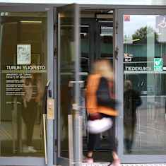 Glass doors leading into the University of Turku, with a blurred image of a person entering the doorway.