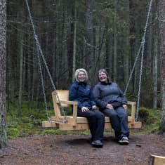Kouvolan kaupungin hyvinvointikoordinaattori Tarja Ala-Mattila ja metsäinsinööri Kirsi Hokkanen istumassa terveysmetsän levähdyspaikan keinussa.