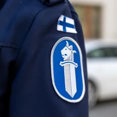 Poliisin virkapuvun tunnus ja Suomen lippu takin hihassa.