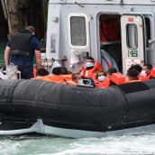 Joukko siirtolaisia pelastusliiveissä laivan kannella.