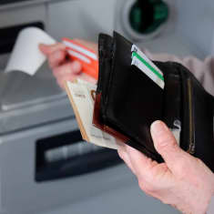 Henkilö pitelee lompakkoa ja seteleitä, ja ottaa toisella kädellä kuittia pikapankkiautomaatista.