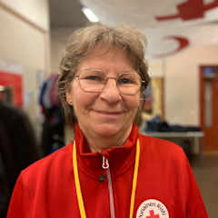 Äldre kvinna med glasögon och klädd i röd tröja med Röda korsets logotyp på. Kvinnan ler och ser in i kameran.