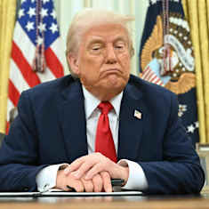 Donald Trumpov sitter i Ovala rummet, lutar sig över skrivbordet och blickar nedåt.