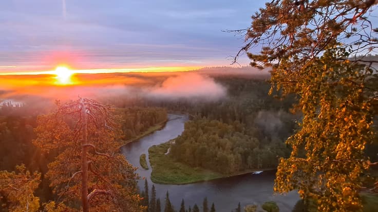 Pähkänänkallion maisemia Kuusamossa. Ounasjoki mutkittelee alhaalla, aurinko nousee usvaisen maiseman ylle. 