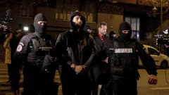 Romanian poliisit taluttavat Andrew Tatea käsiraudoissa kadulla pidätyksen jälkeen.