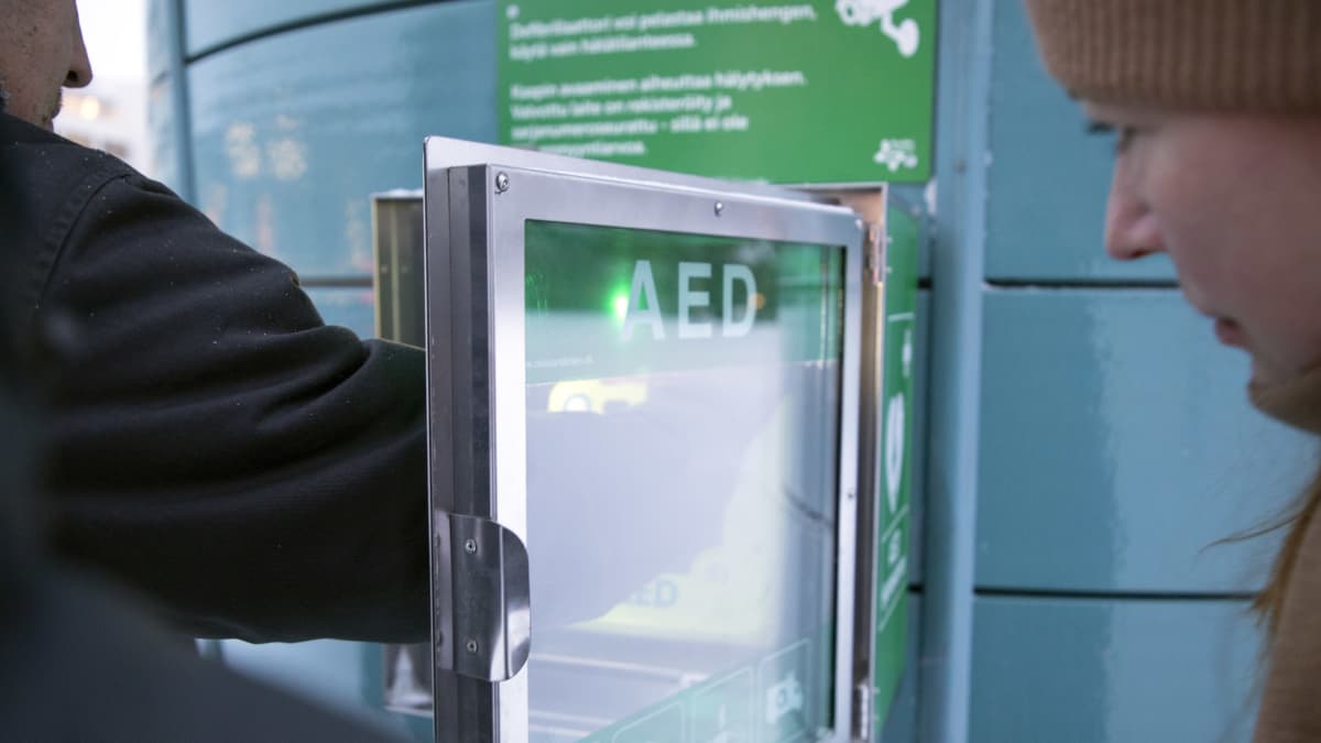 Tamperelaisessa puistossa sijaitseva efibrillaattori, jossa vilkkuu vihreitä valoja. Kuvassa myös ihmisiä tutkimassa laitetta.
