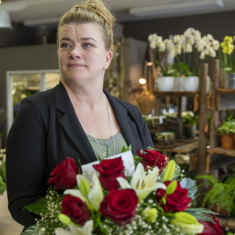 floristimestari Anna Utti seisoo kukkakaupassa kukkalaite käsissään.