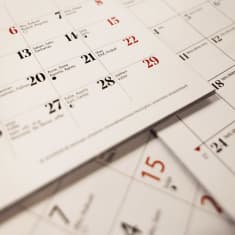 Useita seinäkalenterita päällekkäin pöydällä. Kuvan keskipisteessä sunnuntai 29. päivä.