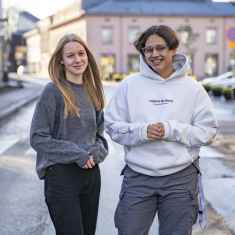 Två ungdomar, en ung kvinna och en kille står ute på en gata med Ekenäs Rådhustorg i bakgrunden. Carolina Friman och Daniel Hassan.