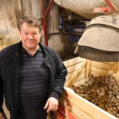 En man står bredvid en halvfull låda med potatis.