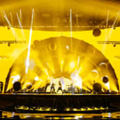 En scen framför en gul bakgrund, på scenen står ett band.